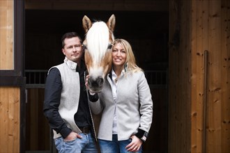 Young couple standing with a Tyrolean Haflinger in front of a stall