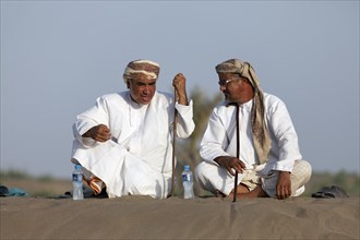 Omanis talking while sitting in traditional clothing