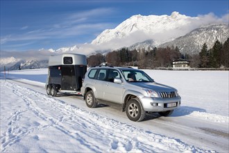 Four wheel drive vehicle towing a horse trailer on a snow-covered road in the mountains