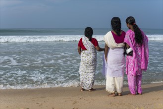 Women standing on the beach facing the sea