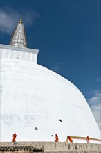 Monks tying a cloth around a large white stupa
