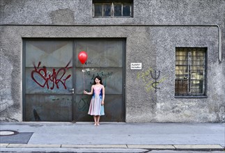 Sad girl holding a red balloon in front of an old garage door