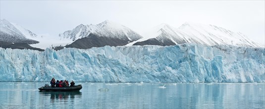 Tourists in a rubber dinghy in front of the rim of the Monacobreen Glacier