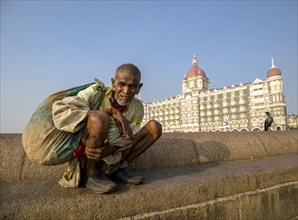 A beggar is sitting in front of the luxurios Taj Mahal Palace Hotel in the suburb Colaba