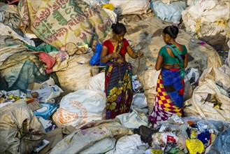 Two women in colorful saris are sorting out garbage for recycling