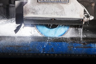 A wet-cutting machine cutting a stone slab