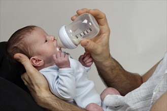 Three-week-old infant boy is fed with the bottle by his father
