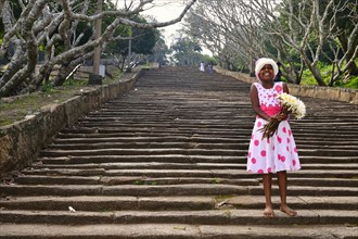Girl with lotus flowers on the stone stairs to the Buddhist temple complex of Mihintale