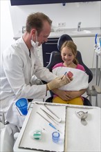 Dentist showing a girl the proper use of a toothbrush