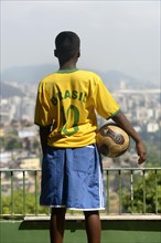 Boy holding a soccer boy and wearing a Brazil jersey while overlooking the centre of Rio de Janeiro