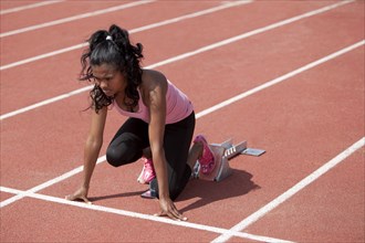 Sporty young woman in starting position on starting blocks