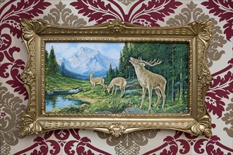 Trashy deer picture in a plastic gold frame on patterned wallpaper