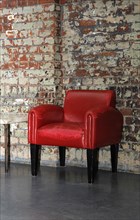 Red armchair in front of an old brick wall