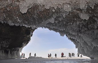 Ice formations and icicles hanging from ceiling in a cave and people walking on frozen Lake Superior