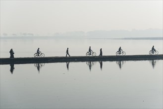 Cyclists and pedestrians crossing the Yamuna river on a dam in the morning