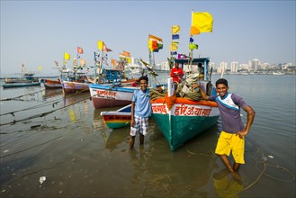 Two fishermen and some fishing boats in front of the skyline of the suburb Churchgate seen across the Back Bay