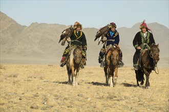 Three Kazakh eagle hunters on their horses on the way to the Eagle Festival in Sagsai