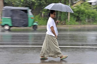 Singhalese woman walking with an umbrella in heavy rain