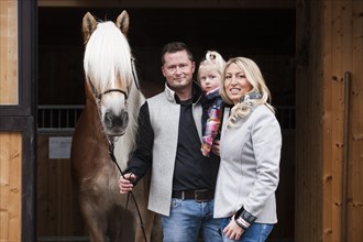 Young family standing with a Tyrolean Haflinger in front of a stall