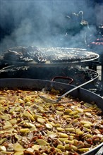 Large pan containing potato stew in front of giant barbecue at the annual All Saints Market in Cocentaina