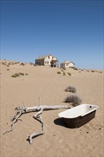Old bathtub and houses of a former diamond miners settlement that is slowly covered by the sand of the Namib Desert