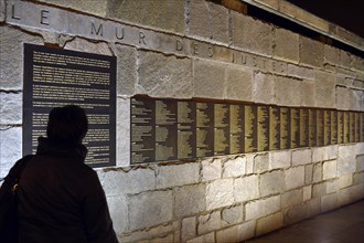 Person standing in front of the Le Mur de Justes plaque at the Memorial de la Shoah