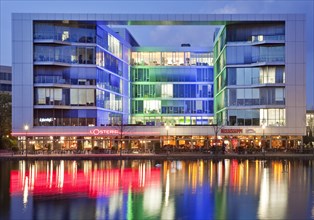 The colourfully lit 'H2 Office' building with restaurants at dusk