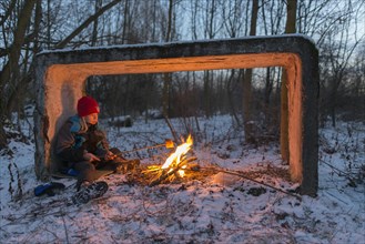 Young boy sitting by the campfire in the snow toasting bread