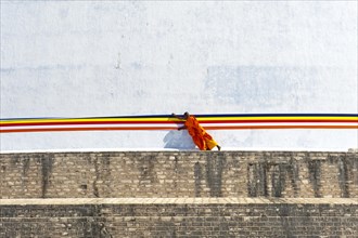 Monk tying a cloth around a large white stupa