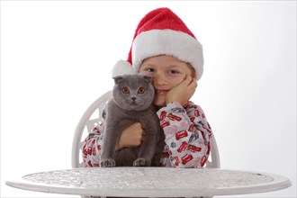 Child wearing a Santa Claus hat holding a gray cat