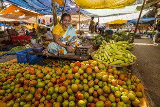 A woman is selling tomatoes and cucumbers at the weekly vegetable market
