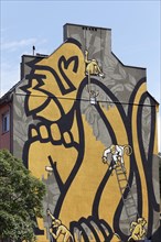 Small monkeys painting a huge monkey on a house wall