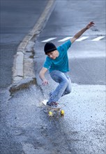 Teenager riding a longboard downhill on a wet street