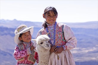 Two girls in traditional dress with an alpaca