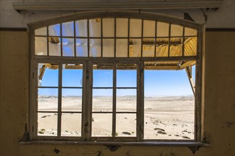 View through a window of an abandoned house in a former diamond miners settlement that is slowly covered by the sand of the Namib Desert
