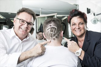 The two hairdressers Gerhard Ostler and Sylvia Ostler posing with a customer who has received a Football World Cup hair tattoo from them