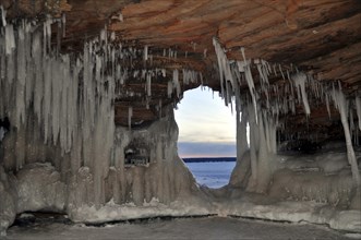 Icicles and ice formations in a cave and view through a natural window onto frozen Lake Superior