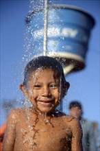 Indian boy of the Xavantes people taking a shower at the water point of a well