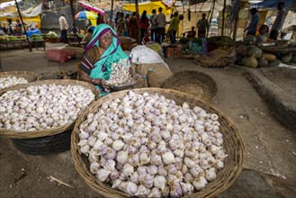 A woman is selling garlic in baskets at the weekly vegetable market