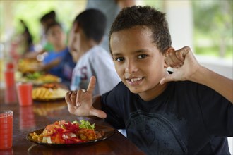 Brazilian boy in front of a full plate of food at the table with other children in a social project for street children