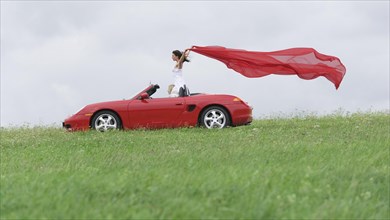 Woman in a convertible letting a red cloth fluttering in the wind