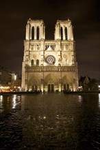 Front view of Notre Dame Cathedral at night with reflections on the wet stones