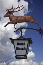 Hanging sign of 'Hotel Hirsch' against a cloudy sky