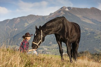 A young woman with a black Hanoverian horse on a mountain meadow in autumn