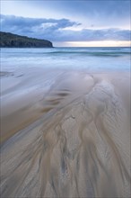Water flows via bizarre structures on the sandy beach into the sea