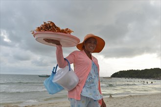 Young Cambodian woman wearing a sun hat selling crabs and shrimps on the beach