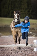 Girl wearing a riding helmet jumping over an obstacle with a pony