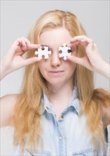 Woman holding two white puzzle pieces in front of her eyes