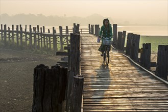 Girl with tanaka on her face riding a bicycle on a teak bridge