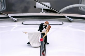 Figures of a wedding couple on the hood of a white vintage car